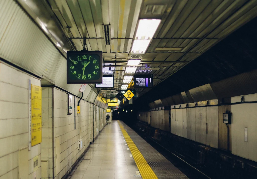 Empty underground platform in Japan with a green clock, Japanese signs, and a yellow tactile safety strip along the track edge.