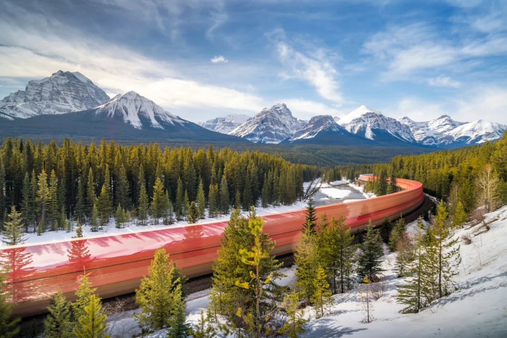 A red freight train bends through snowy pines with the Canadian Rockies towering behind—classic Morant’s Curve along the Bow River in Banff National Park.