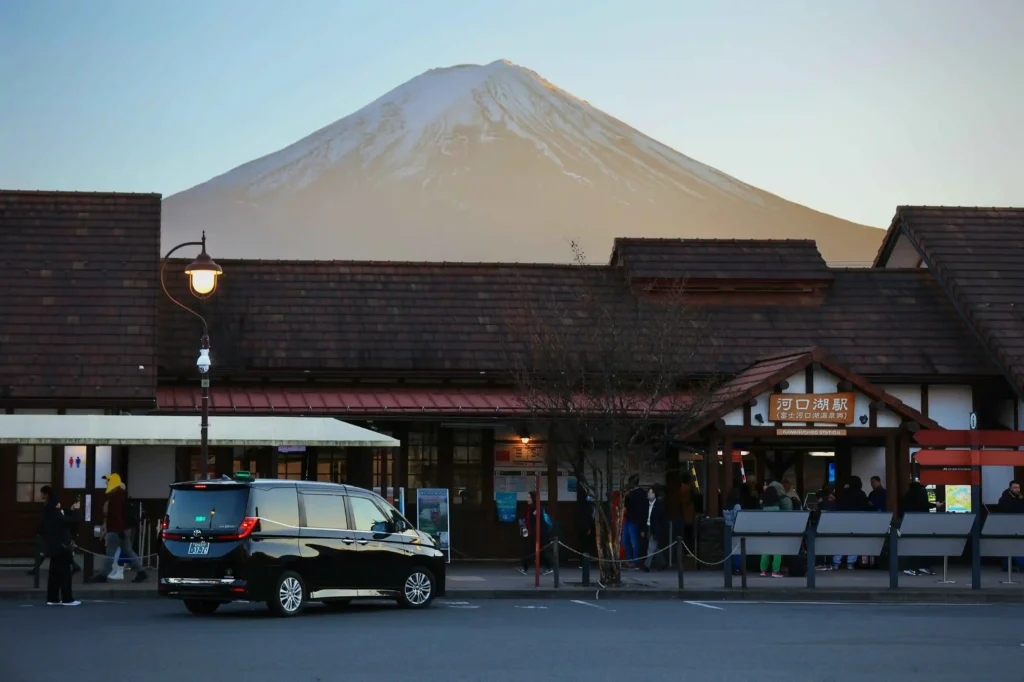 Mount Fuji under a clear blue sky above Kawaguchiko Station’s gabled roof, with a round clock centered on the facade.