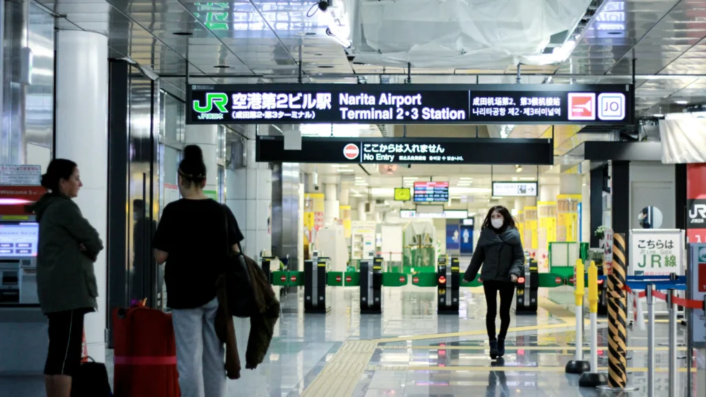 Interior signage for “Narita Airport Terminal 2·3 Station” with JR gates and travelers.