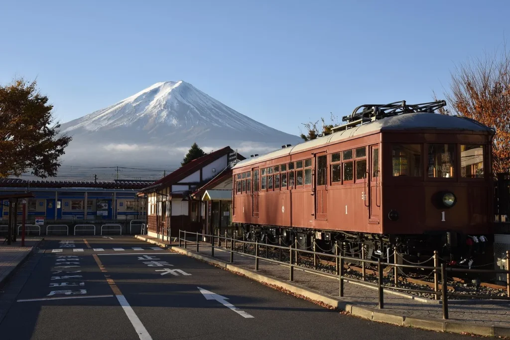 Historic brown electric railcar at a small Japanese station with snow-capped Mount Fuji in clear morning light.