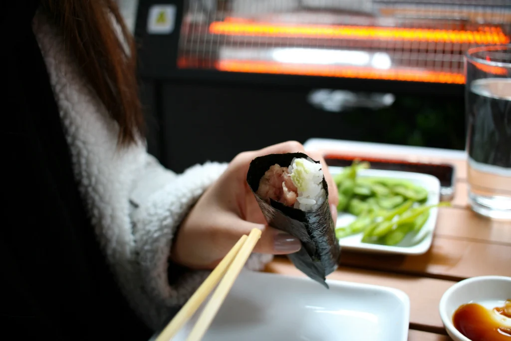 Hand roll sushi wrapped in nori with edamame and soy sauce on the table.